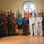 A formal group photograph taken at the Naval Small Craft Instruction and Technical Training School (NAVSCIATTS), showing military personnel in various uniforms alongside a civilian woman in a blue blazer. The group consists of approximately 12 individuals representing multiple nations, as evidenced by the diverse military uniforms and international flags visible in the background. This appears to be an official diplomatic or training program event.
