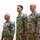 Three U.S. Army soldiers in Army Combat Uniform (ACU) digital camouflage pattern are standing at attention in what appears to be an indoor military ceremony or formal event. All three wear 'U.S. ARMY' chest tapes and unit shoulder patches, suggesting this may be a change of command, promotion, or award ceremony. They are aligned in a row facing the same direction with a neutral background behind them.