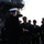 Japanese prime minister visits USS Ronald Reagan A formal military gathering on the deck of what appears to be a large naval vessel, likely an aircraft carrier, indicated by the superstructure and yellow 'E' marking visible in the background. A group of naval officers in dress uniforms, along with civilians, are assembled facing a senior officer whose back is to the camera. The setting suggests an official visit, briefing, or welcoming ceremony.