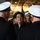Japanese prime minister visits USS Ronald Reagan A civilian man in dark clothing is engaged in conversation with naval officers wearing white-topped dress uniform caps. The setting appears to be an indoor military facility, possibly the hangar deck of a naval vessel. Multiple uniformed personnel are visible in the background, suggesting an official visit or ceremony.
