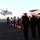 Japanese prime minister visits USS Ronald Reagan A military ceremony is taking place on the flight deck of an aircraft carrier, where naval officers in dress uniforms and deck crew in colored jerseys are lined up along a red carpet awaiting the arrival of a helicopter. The helicopter, marked with the number '53' and appearing to bear Japanese Maritime Self-Defense Force markings, is approaching to land. A fixed-wing aircraft, likely an E-2 Hawkeye (number 601), is visible parked on the deck in the background.