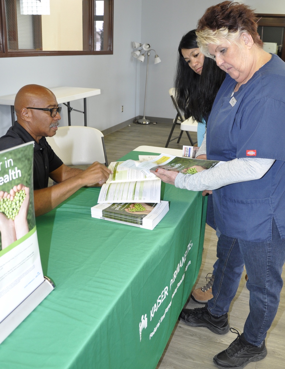 Dorothy Adams, lead store associate and Mercy Jauss, store associate, inquire about Kaiser Permanente benefits with Greg Campbell, Kaiser enroller during a Benefits Fair held aboard Marine Corps Logistics Base Barstow, Calif., Oct. 28