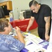 Adrian Castillo, meat cutter at the base commissary, inquires about benefit options with JoAnne Rowles, a contract representative for Government Employees Health Association (GEHA) at the Benefits Fair held aboard Marine Corps Logistics Base Barstow, Cali