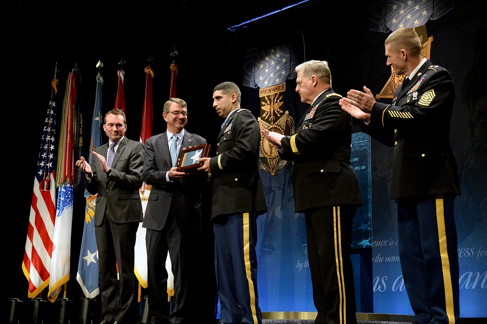 Secretary of defense presents retired Army Capt. Florent Groberg with a flag during the Medal of Honor Hall of Heroes induction ceremony