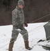 Soldier shovels snow on tent to secure it
