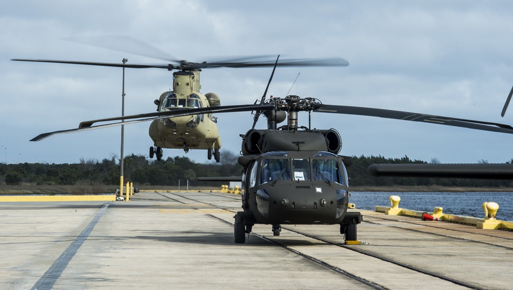 A CH-47 Chinook lands behind a UH-60 Black Hawk on a cargo ship.