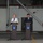 German, Turkish leadership meet to discuss coalition forces partnerships Two officials stand at separate podiums during a joint press conference in what appears to be a military hangar or facility. The German flag is displayed on the left and the Turkish flag on the right, indicating a bilateral meeting between German and Turkish representatives. Both podiums feature identical blue circular emblems, suggesting an official institutional setting.
