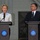German, Turkish leadership meet to discuss coalition forces partnerships Two individuals are standing at separate podiums giving a joint press conference or official statement. The podiums display identical official seals with Turkish text reading '10 UNCU TANKER ÜS KOMUTANLIĞI' (10th Tanker Base Command), indicating a Turkish military air base setting. A woman on the left is speaking into a microphone while a man on the right listens.