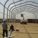 D-Cell installs wiring on an arch for a Large Area Maintenance Shelter