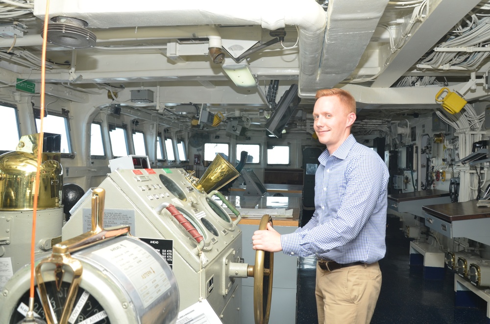 Alec Johnson, a military legislative assistant, poses with the helm of USS Frank Cable (AS 40) during a Congressional tour
