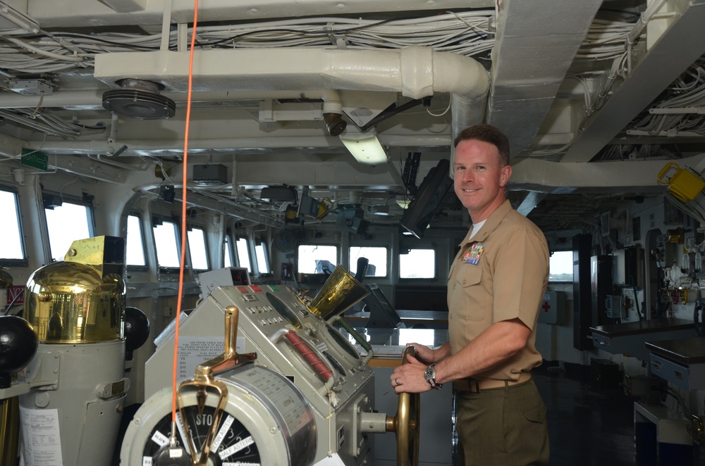 Maj. Christopher Shore, member of the Joint Program Office Forward, poses with the helm of USS Frank Cable (AS 40) during a Congressional tour