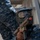 A person wearing blue digital camouflage uniform and a protective paintball/training mask is holding a tan/FDE-colored training weapon with a red barrel plug indicator. A shoulder patch with Arabic script is visible on the uniform, suggesting affiliation with a Middle Eastern military or naval force. The scene appears to be a military training exercise involving simulated combat scenarios.
