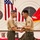 Two U.S. Marine Corps personnel in service uniform (tan shirt, olive trousers) are shaking hands during what appears to be a marksmanship awards ceremony. The senior Marine on the left is presenting an item to a Sergeant on the right, with trophies, plaques, and shooting targets visible in the background. The setting appears to be an indoor gymnasium or assembly hall decorated for a formal military ceremony.
