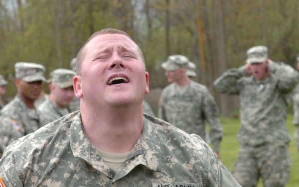 A U.S. Army Sergeant named Peet is captured in an outdoor setting with an intense emotional expression, head tilted back and mouth open. He is surrounded by other soldiers in ACU (Army Combat Uniform) camouflage pattern uniforms in what appears to be a field training or competition event. The background shows multiple soldiers observing or participating in the activity.