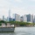 A U.S. Navy warship bearing hull number 99 is sailing in New York Harbor with sailors in white dress uniforms manning the rails in a formal ceremonial formation. Behind the vessel, Governors Island is visible with its historic brick buildings and tree line. The Lower Manhattan skyline, prominently featuring One World Trade Center, forms the backdrop.