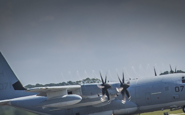 A military C-130 Hercules turboprop transport aircraft is captured during takeoff or landing on a runway. The aircraft bears tail code 'BH 807' and fuselage number '071', indicating it is a US Marine Corps aircraft. The image was taken with a telephoto lens, showing heat shimmer and motion blur consistent with an active runway environment.
