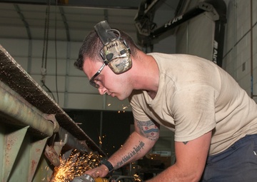 Metal Worker Grinds Down Jutting Piece on Trailer