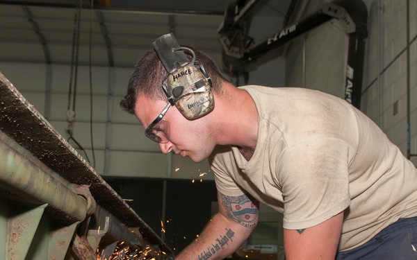 Metal Worker Grinds Down Jutting Piece on Trailer