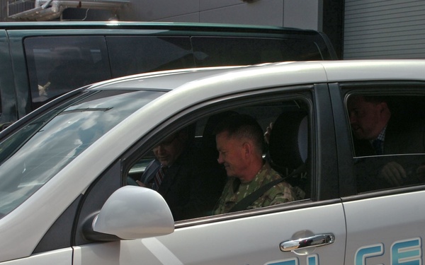 A white Chevrolet fuel cell vehicle with a distinctive blue water-themed graphic wrap is shown with occupants inside. The vehicle displays 'FUEL CELL' text and the Chevrolet bowtie logo prominently on its side. At least three occupants are visible, including one person in military camouflage uniform in the front passenger seat.