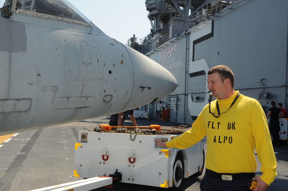 Aviation Boatswain's Mate 1st Class Shawn Conway gives hand signals while Sailors move a harrier aircraft on the flight deck of the amphibious assault ship USS Bataan (LHD 5).