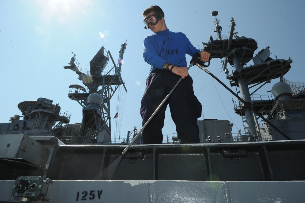 Airman Recruit Lane Sullivan uses a power washer on the flight deck of the amphibious assault ship USS Bataan (LHD 5).