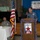 A formal military/civic event called 'Operation Lone Star VIP Day 2016' is taking place in an indoor venue. A civilian speaker addresses the audience from a decorated podium while two military officers in Army combat uniforms are seated at a table to his left. A banner credits 'Double Y Orchard' as a sponsor of the event.