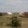 Fighting our nation's wars: one 50lb round at a time The image shows multiple M1 Abrams main battle tanks conducting a live-fire exercise on an open training range. At least one tank in the middle distance is visibly firing its main gun, with a muzzle flash and smoke clearly visible. The foreground tank is marked with the number '22' and is moving across the terrain, kicking up dust.