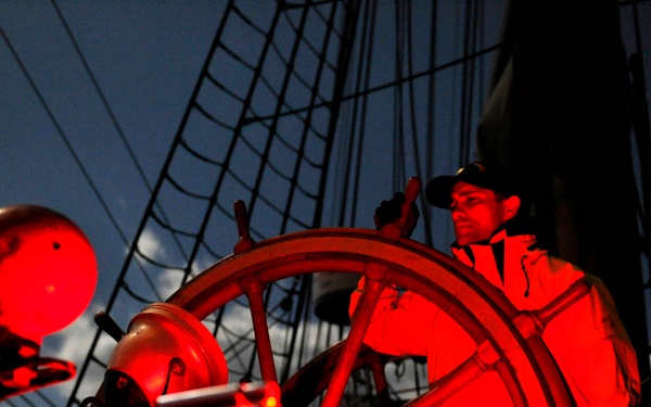 Coast Guard Cutter Eagle crewmember mans the helm under a full moon