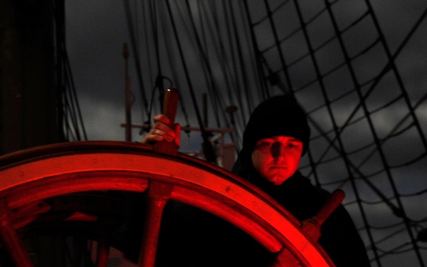 Coast Guard Cutter Eagle crewmember mans the helm under a full moon