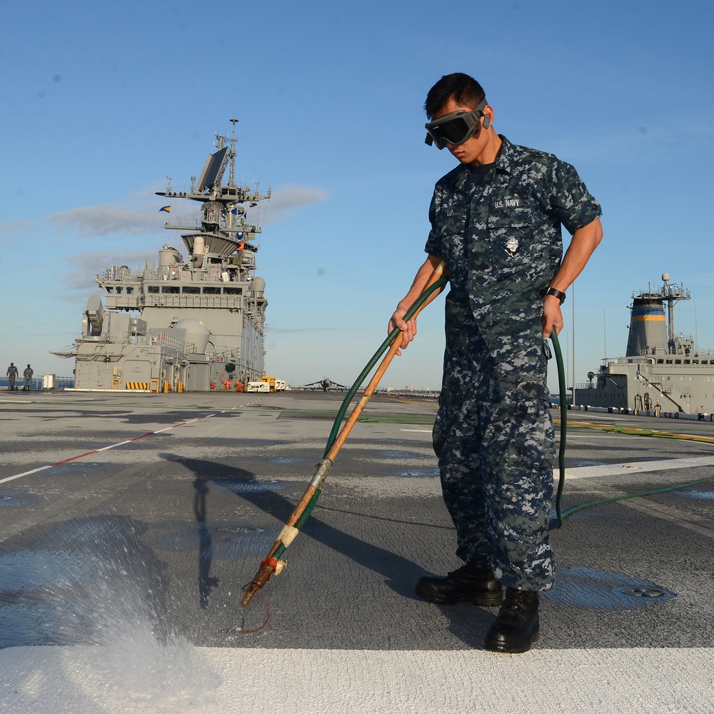 NORFOLK, Va. (AUG. 22, 2016) -- Airman Bo Lu, a Chinese immigrant,uses compressed air to remove water from pad-eyes on the flight deck of the amphibious assault ship USS Bataan (LHD 5).