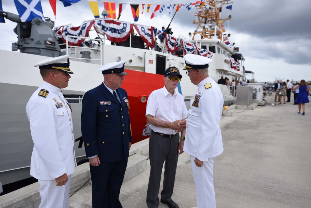 Rear Admiral Scott Buschman, Commander of the Coast Guard 7th District, presents Walt Slater, U.S. Navy Retired Motor Machinist's Mate 3rd Class, with a coin after the commissioning ceremony of the 18th Fast Response Cutter.