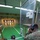 USAG Benelux Soldiers qualify with brand new M4A1 carbines. Two military personnel are at an indoor shooting range. One soldier in ACU (Army Combat Uniform) is in the prone position aiming downrange, while a second soldier in MultiCam/OCP uniform kneels nearby using binoculars to observe the targets. The facility is a well-lit indoor range with multiple target lanes, lane dividers, and safety signage.
