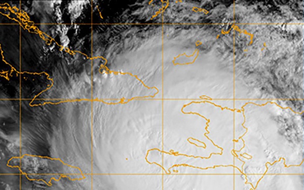 This is a satellite imagery capture of a large tropical cyclone (hurricane) over the Caribbean Sea, with orange geographic boundary overlays identifying regional landmasses. The storm system displays a well-defined spiral banding structure with a discernible eye or eye-wall region centered near Hispaniola (Haiti/Dominican Republic). Latitude grid lines are visible, with markers indicating approximately 16°N and 20°N latitude.
