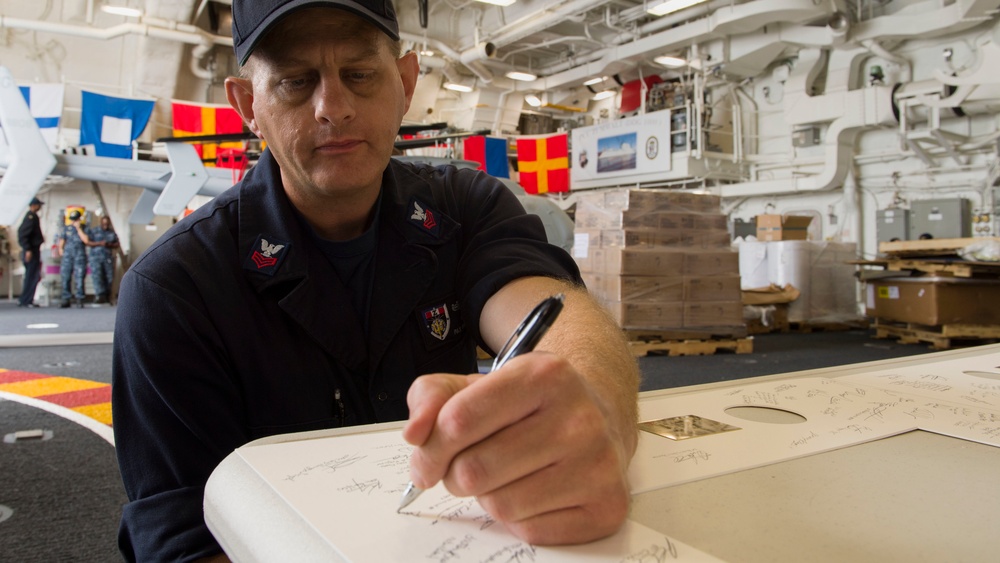 USS Zumwalt Sailor signs a board for presentation to ship's sponsor family