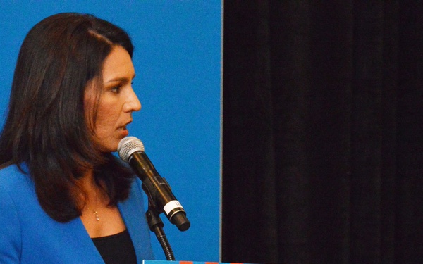 A woman in a blue blazer is speaking at a podium during a Transition Summit event. The podium displays branding for 'Hiring Our Heroes,' an organization focused on military veteran employment. She is speaking into a microphone mounted on the podium.