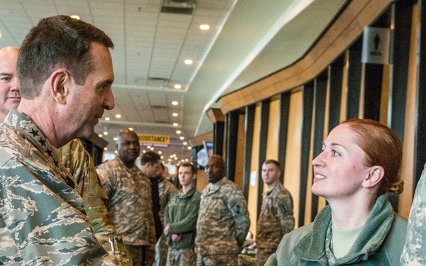 A senior U.S. Air Force officer in Airman Battle Uniform (ABU) with general officer stars is shaking hands with a U.S. Army female soldier wearing a green fleece jacket with a name tape reading 'HIGGINS' and a Staff Sergeant rank insignia. The setting appears to be an indoor military event or reception area with multiple service members standing in the background. The interaction suggests a formal greeting or recognition ceremony.