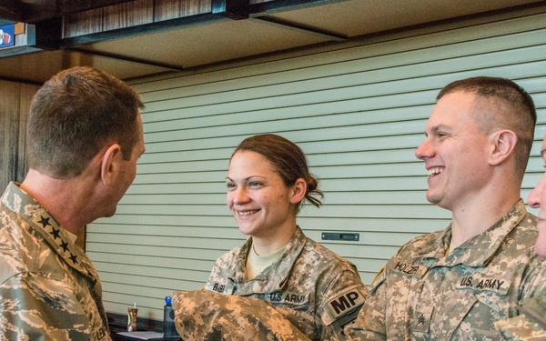 A senior military officer in Air Force ABU (Airman Battle Uniform) is shaking hands with U.S. Army soldiers in ACU (Army Combat Uniform) at what appears to be an indoor military event or gathering. The officer displays general officer rank insignia (stars) on his collar. Three Army soldiers are visible, including one with an 'MP' (Military Police) patch and another with a name tape reading 'HOLZER' and a Specialist rank insignia.