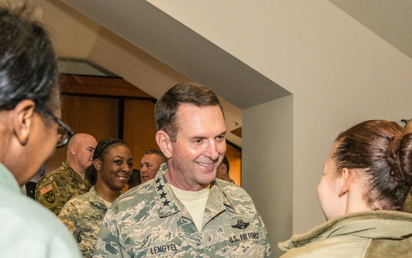 A U.S. Air Force general officer identified by his name tape as 'LENGYEL' is engaged in a friendly conversation with a group of people in what appears to be an indoor military or official setting. He is wearing the Airman Battle Uniform (ABU) with general officer rank insignia visible on his shoulders. The atmosphere appears informal and social, with multiple people smiling and interacting.