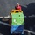 Moving Supplies An aerial view of a person in a red flight deck suit and helmet operating a yellow forklift on what appears to be a military aircraft carrier deck. The forklift is transporting a large pallet loaded with cases of Mountain Dew and Pepsi beverages. The image captures a resupply or provisioning operation on the ship's flight deck.