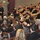170118-N-DE005-004 A speaker in dark civilian clothing stands at the front of an auditorium-style room addressing a large mixed audience of military personnel in uniform and civilians in business attire. The setting appears to be a formal briefing or lecture at a military installation or conference facility. The audience is seated in tiered rows facing the presenter.