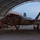 Lightning II strikes Iwakuni, F-35B arrives A U.S. Marine Corps F-35B stealth fighter jet is positioned inside an arched hangar structure during dusk or early morning hours. Ground crew personnel are conducting pre-flight or post-flight checks around the aircraft. The aircraft displays green navigation/status lights and bears USMC markings including a star-and-bar insignia and unit designation.