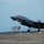 Lightning II strikes Iwakuni, F-35B arrives A U.S. Marine Corps F-35B Lightning II stealth fighter jet is captured during a landing or takeoff on a runway at dusk or dawn. The aircraft bears USMC markings including a star-and-bar insignia and squadron designation 'VMFA-121' on the fuselage. All three landing gear are deployed and green navigation lights are visible on the aircraft.