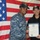 170120-N-BK203-954 Two U.S. Navy personnel are posing together in front of an American flag while holding a certificate. The individual on the left is wearing Navy Working Uniform (NWU) digital camouflage, while the individual on the right is wearing a black fleece jacket. Both are wearing Navy-issued caps with ship or command insignia.