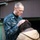 USS Bonhomme Richard (LHD 6) Sailors participate in a Food Drive A U.S. Navy servicemember named Hammond, wearing Navy Working Uniform (NWU) digital camouflage, places his hand on the bowed head of a civilian. The gesture appears to be a blessing or prayer, consistent with the role of a military chaplain. The setting appears to be outdoors near a building structure.