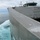170120-N-OH262-776 A close-up view of the hull and superstructure of a large military or government vessel underway at sea, photographed from an elevated angle along the starboard side. The aluminum-hulled ship appears to be a high-speed catamaran or similar multi-hull vessel, showing significant wear and weathering on its hull plating. The vessel is moving through open ocean, generating visible white wake and disturbed turquoise water alongside the hull.