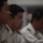 Japan Ground Self-Defense Force tours Marine Logistics Group facilities Three individuals in military-style uniforms are seated in a row, appearing to be attending a briefing, meeting, or formal event. The foreground subject is in sharp focus wearing a light-colored uniform with visible rank insignia on the collar and service ribbons on the chest. The two individuals behind are progressively out of focus due to shallow depth of field.