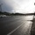 Camp Pendleton flood 2017 A wet road scene showing what appears to be a road closure or checkpoint, with orange traffic cones and barriers blocking the roadway ahead. A police vehicle is visible on the left side of the road, along with a white civilian car. The scene is set against a backdrop of green hills under a dramatic, partly cloudy sky with strong backlighting from the sun.