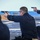 170119-N-RM689-732 The image shows military or law enforcement personnel conducting a firearms qualification or training exercise on what appears to be the deck of a naval vessel at sea. The primary subject is kneeling in a shooting stance, aiming a semi-automatic pistol downrange while wearing safety glasses and ear protection. At least two other personnel are visible, also armed and participating in the exercise.
