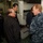 Amphibious Squadron 11 Hosts Tour Aboard USS Bonhomme Richard (LHD 6) Two U.S. Navy personnel in blue digital camouflage (NWU Type I) uniforms are conducting what appears to be a tour or briefing for a group of civilian visitors, likely of East Asian descent, inside a naval vessel. The setting appears to be a berthing compartment or interior passageway of a ship, with bunk beds visible in the background. The interaction appears formal and informational in nature.