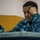 170119-N-OY799-053 A U.S. Navy sailor in Navy Working Uniform (NWU Type I blue digital camouflage) is seated at a desk, appearing to be in deep concentration or thought. The sailor's name tape partially reads '-WARE' and 'U.S.' branch tape is visible on the uniform. The setting appears to be a classroom or briefing room environment.